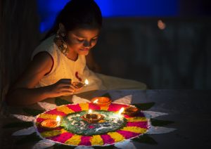 Girl making Rangoli and decorating with Oil lamps for Diwali