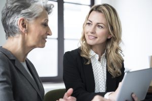 Mid adult woman with tablet smiling at mature colleague