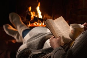 Woman reads book near fireplace